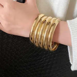 Nahaufnahme glänzender goldfarbener Armreifen am Handgelenk, 5er-Set stilvoller Ringe.