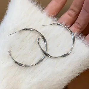 Close-up view of elegant twisted silver hoop earrings resting on soft white faux fur.