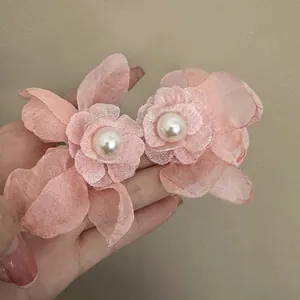 Close-up detail of pink mesh flower earrings with central white pearls and silver needles.