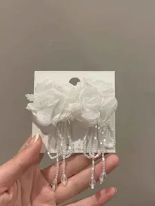 Close-up detail of white mesh flower earrings featuring elegant long beaded tassels