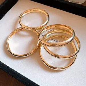 Stapel von fünf minimalistischen, goldfarbenen, glatten runden Metallarmreifen auf einem Tablett