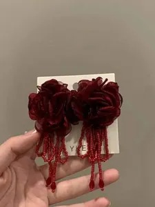 Macro detail of red mesh flower earrings featuring long bead tassels on a white card