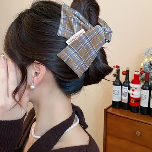 Close-up of a plaid fabric hair claw clip with a Handmade tag worn by an Asian model