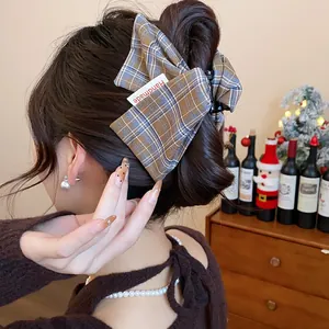 Elegant plaid fabric bow hair claw clip shown on a woman's hair bun in a cozy setting