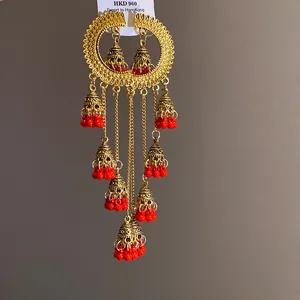 Close-up detail of ornate gold bell tassel earrings accented with vibrant red bead charms