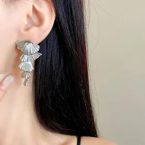 Close-up of elegant silver-colored multi-layered fan-shaped drop earrings worn by a model.