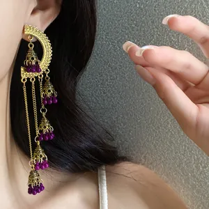 Close-up detail of vintage ethnic style gold tassel earrings with purple beads and bells on model