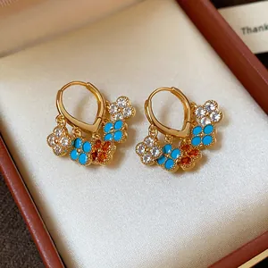 Close-up of gold-plated flower dangle earrings with zircons and blue enamel details.