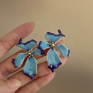 Primer plano de pendientes de flores de esmalte azul con detalles dorados.