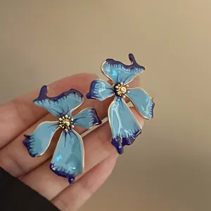 Detalle de pendientes de botón con flor azul irregular, borde dorado y acabado esmaltado