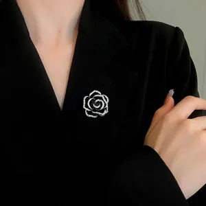 Elegante spilla camelia nera con accenti di zircone scintillanti su un blazer nero.