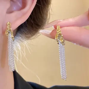 Close-up of silver needle earrings with gold pleated tops and silver tassel chains.
