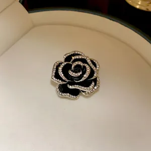 Elegante spilla a camelia nera con bordi in zircone, mostrata in confezione di lusso.