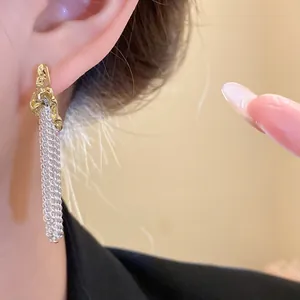 Close-up detail of stylish gold pleated C-shaped earrings with long silver mesh tassels