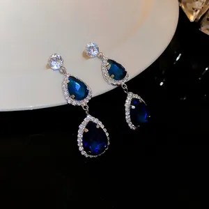 Elegant silver needle earrings with deep blue teardrop stones and micro-pave crystals.