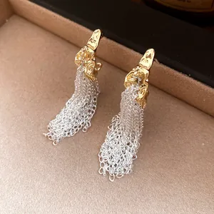 Detailed view of golden wrinkled C-shape stud earrings with elegant silver chain tassels