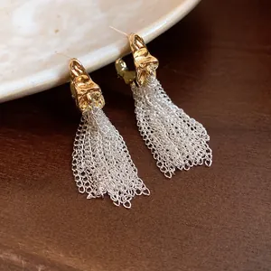Elegant gold C-shape stud earrings with silver chain tassels on a dark wood background.