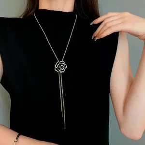 Dettaglio di un ciondolo a forma di camelia con zirconi su una lunga collana argentata.