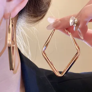 Dettaglio di grandi orecchini a cerchio geometrici a rombo dorati per un look minimalista