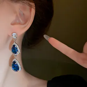 Close-up of elegant teardrop earrings featuring deep blue crystals and silver pavé accents.