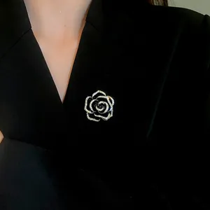 Dettaglio di un'elegante spilla a camelia in smalto nero con strass su giacca nera