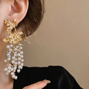 Eleganti orecchini a foglia d'acero dorata con nappe di perle bianche a cascata su una modella.