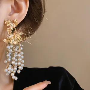 Dettaglio orecchini foglia d'acero dorati con nappe in perle bianche su modella