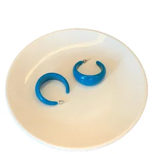 Vibrant blue acrylic C-shaped hoop earrings with steel needles on a white plate