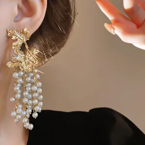 Vista dettagliata di orecchini a foglia d'acero dorati con eleganti nappe di perle bianche