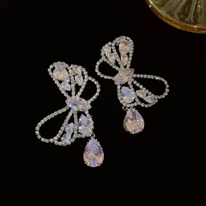 Detailed view of elegant bow earrings with shimmering teardrop zircons against a black background.
