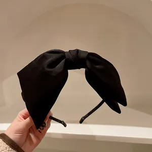 Dettaglio di un cerchietto con fiocco in raso nero stile vintage dalla trama elegante.