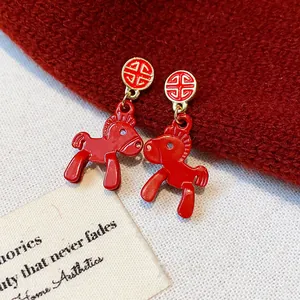 Close-up of vibrant red pony earrings with gold traditional studs on a red knitted background
