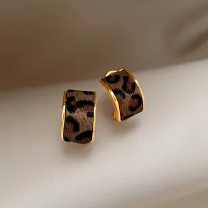 Close-up detail of stylish gold-toned C-shaped hoop earrings with leopard print fabric inlay