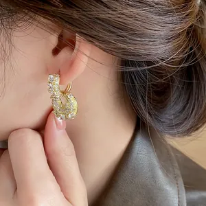 Detailed view of gold-plated U-shaped zircon bag earrings worn on model's ear.
