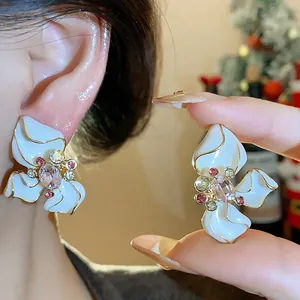 Detailed close-up of elegant white enamel flower stud earrings with a pink rhinestone