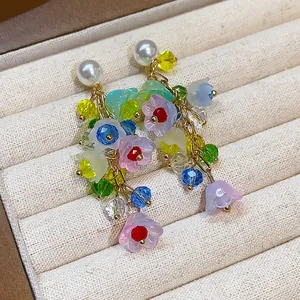 Close-up of colorful resin flower tassel earrings with pearl studs on a jewelry tray.