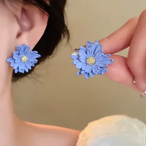 Close-up view of elegant blue daisy flower stud earrings with yellow stamens on ear