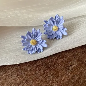 Detailed view of periwinkle blue flower earrings with gold textured centers and silver needles.