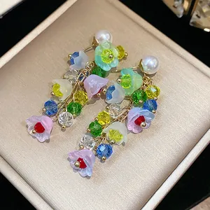 Close-up of colorful resin flower tassel earrings with pearls on gold display box