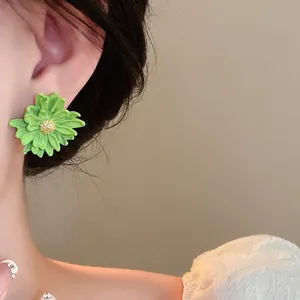 A close-up view of a sweet green flower stud earring with gold center worn on an ear