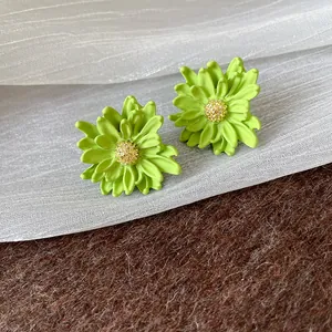Elegant green flower stud earrings with golden stamens placed on white sheer fabric backdrop