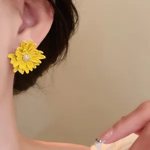 Close-up of a yellow flower stud earring with glitter center on an ear.