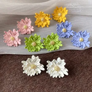 Close-up of colorful flower stud earrings with golden centers on textured background.