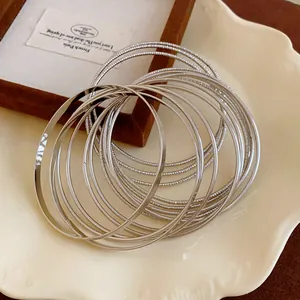 Detailed close-up of multiple thin silver metal bangles stacked on a scalloped ceramic plate.