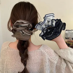 Oversized striped fabric scrunchies shown on a braided ponytail and held by a model.