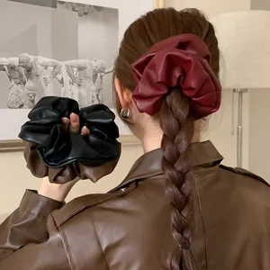 Close-up of oversized retro leather scrunchies in wine red and black on a braided ponytail