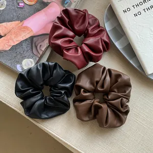 Detailed macro view of three faux leather scrunchies in maroon, black, and brown colors