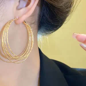 Detailansicht stilvoller mehrlagiger goldener strukturierter Creolen an einem Model.