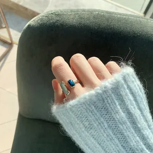 Primo piano di un anello aperto geometrico in smalto blu indossato con un maglione blu