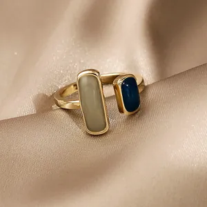 Primo piano di anello geometrico dorato con dettagli rettangolari in smalto blu e salvia